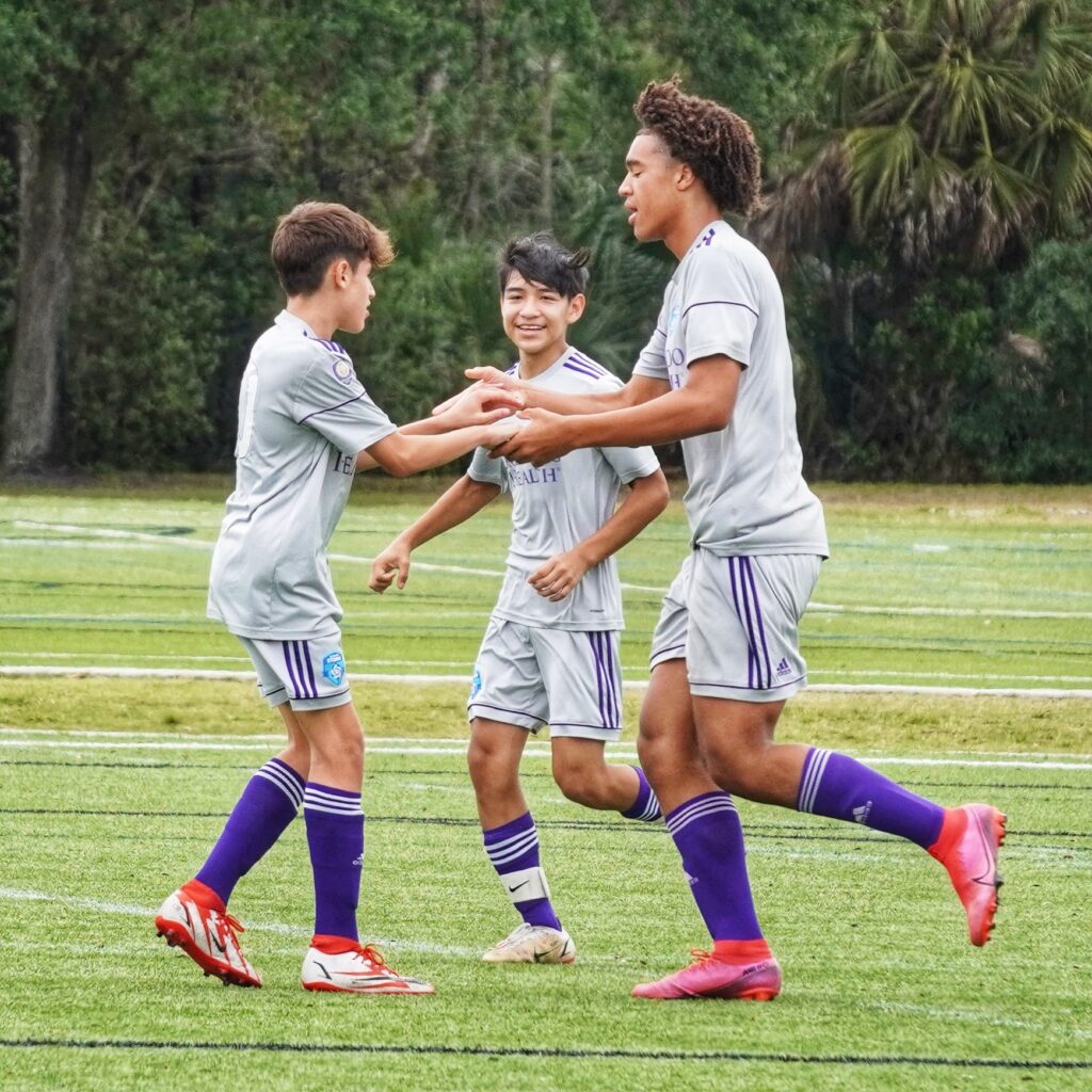 Three soccer teammates high-fiving each other while playing soccer